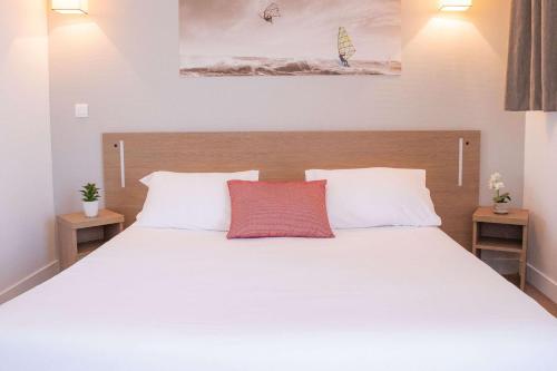 a bedroom with a large white bed with a red pillow at Comfort Aparthotel Cannes Mandelieu in Mandelieu-la-Napoule