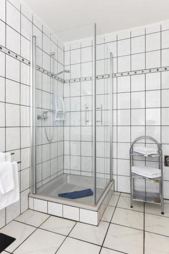 a shower in a white tiled bathroom with a chair at Haus Hafeneck FeWo Ebbe in Bensersiel