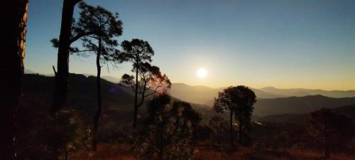 a sunset in the mountains with trees in the foreground at HIll Queen Homestay Chaukori By StayApart in Chaukori