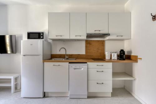 La cuisine blanche est équipée d'un évier et d'un réfrigérateur. dans l'établissement Le Cyperus Appartement avec Terrasse et Wifi, à Peyriac-de-Mer