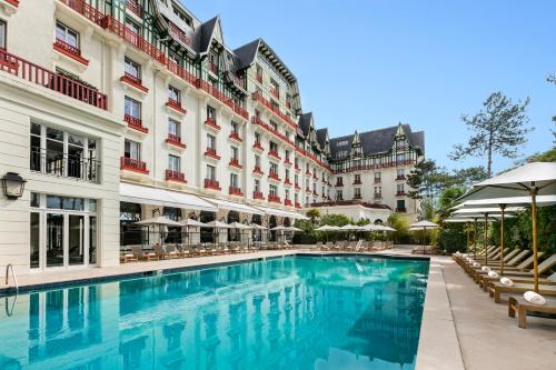 - une piscine en face d'un bâtiment avec des chaises et des parasols dans l'établissement Hôtel Barrière L'Hermitage, à La Baule