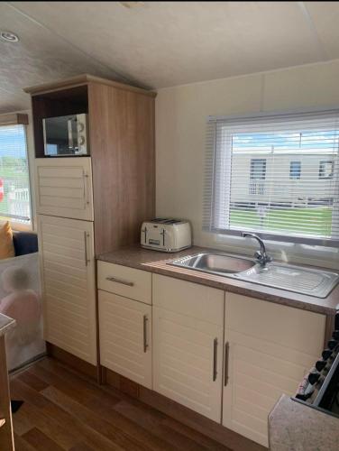 a small kitchen with a sink and a microwave at 8 Berth 3 bed caravan Golden palm ML9 in Chapel Saint Leonards