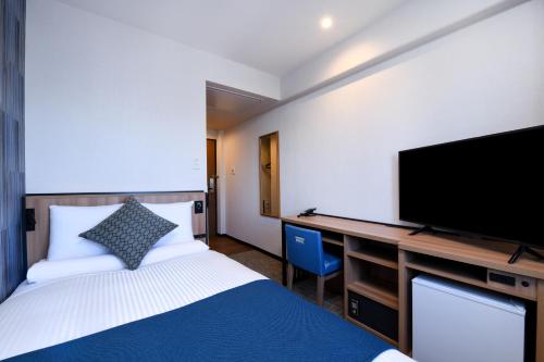 a bedroom with a bed and a desk with a flat screen tv at HOTEL MYSTAYS Atsugi in Atsugi