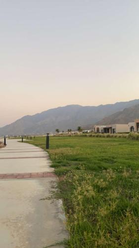 a sidewalk next to a field with mountains in the background at Sifah seaCottage in Muscat