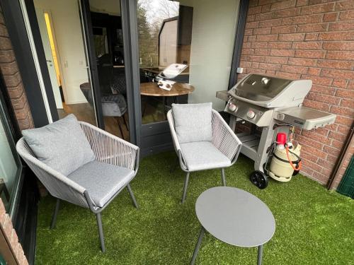two chairs and a grill on a patio with grass at Fantastische Hotel Alternative in Oststeinbek
