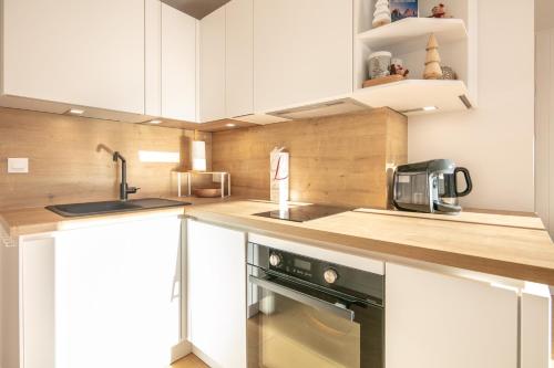 une cuisine avec des armoires blanches, un évier et une cuisinière dans l'établissement Le Murmure des Flocons - Vostok Zodiaque, à Villarembert