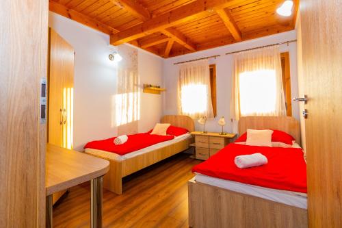 a bedroom with two beds with red sheets and wooden ceilings at Tisza Panzió és Apartman in Tiszaújváros