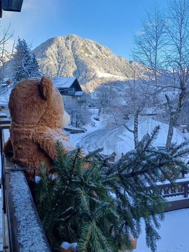 a teddy bear sitting on a ledge with a christmas tree at Chalet Appart'Hôtel l'Eau Vive in Saint-Nicolas-la-Chapelle