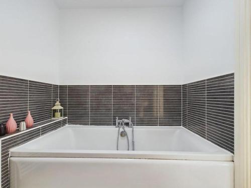 a white bath tub in a bathroom with black tiles at Sleeps6- FamilyFriendly- FreeParking- 3Br in Stafford