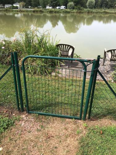 a gate with two chairs in front of a lake at La maison de l'étang in Saint-Georges-sur-Arnon