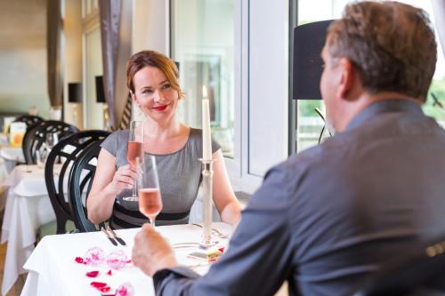 a man and a woman sitting at a table with wine glasses at Vitalia Seehotel in Bad Segeberg