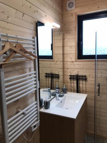 La salle de bains est pourvue d'un lavabo blanc et de 2 fenêtres. dans l'établissement Le chalet de Lenny- spa- borne recharge- wifi, à Luçay-le-Mâle
