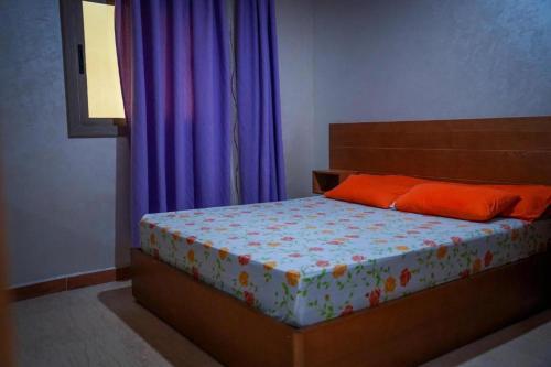 a bedroom with a bed with orange pillows and purple curtains at appartements Al Amri akchour in Chefchaouene