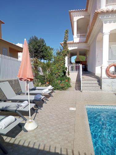 a villa with a swimming pool with lounge chairs and an umbrella at Vivenda Luz - Jacuzzi & Swimming Pool in Albufeira