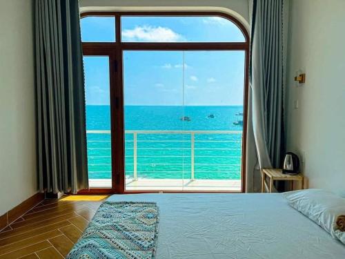 a bedroom with a large window looking out at the ocean at Coco Bay Hon Son in Lai Sơn