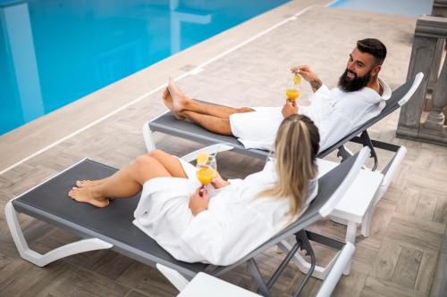 two people sitting in chairs by a pool with drinks at Hotel Mio City in Kula