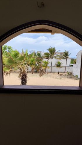 a window view of a beach with palm trees at Espaço Akronos Residence in Canoa Quebrada