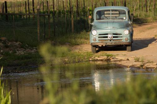 an old car parked on a dirt road next to water at De Kombuys in Oudtshoorn