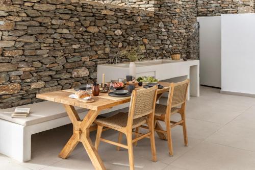 a dining room table with chairs and a stone wall at GN7 Villas in Kithnos