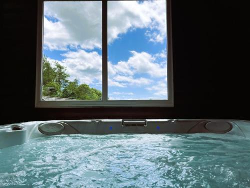 a bath tub with a window in a bathroom at Hop Loft-Barn Conversion, with access to Pool & Hot Tub-at Fox Valley Cottages in Looe