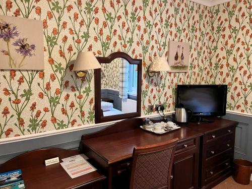 a room with a desk with a mirror and a television at Ramnee Hotel in Forres