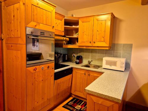 - une cuisine avec des placards en bois et un four micro-ondes blanc dans l'établissement Arc 1950 - Appartement 2 chambres - 6 personnes - 53m2-ski aux pieds - Les Sources de Marie, à Arc 1950