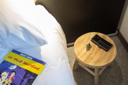 a table with a remote control on it next to a bed at greet Hôtel Montbéliard in Montbéliard