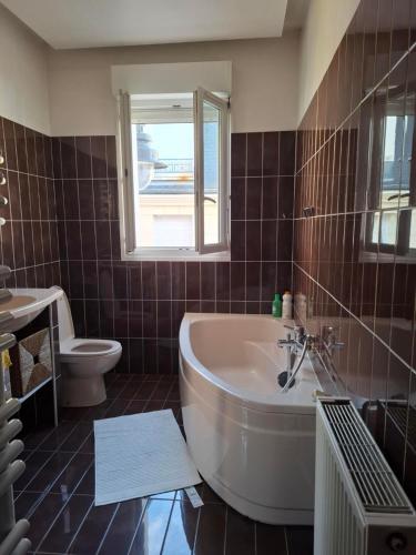 a bathroom with a tub and a toilet and a window at F2 cosy aux portes de Paris - 6 min de RER de Paris Gare de Lyon in Maisons-Alfort