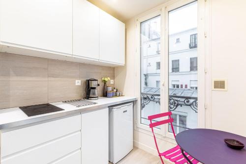 une cuisine avec des armoires blanches, une table et une fenêtre dans l'établissement GuestReady - Studio Parisien près des attractions, à Paris