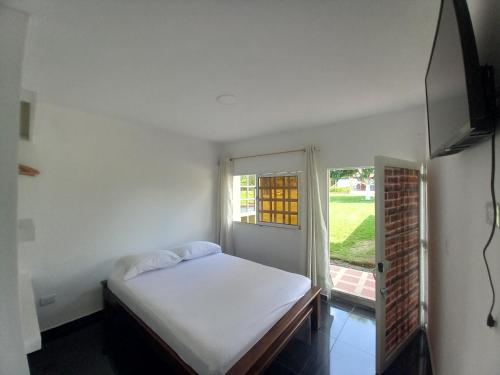 a white bedroom with a bed and a window at Alojamiento Sol de Maíz in Quimbaya