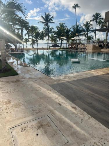 a large swimming pool with palm trees and the ocean at Apartment in Playa Nueva Romana in San Pedro de Macorís