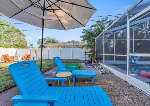 a patio with blue chairs and an umbrella and a pool at 3BR Sunshine Retreat with Heated Pool, Cold Plunge and Games in Bradenton