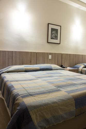 a large bed with a blue plaid blanket on it at Hotel Estação 101 - Itajaí in Itajaí