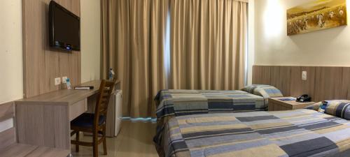 a hotel room with two beds and a desk and a television at Hotel Estação 101 - Itajaí in Itajaí
