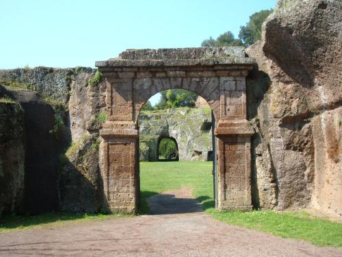an archway in a stone wall with a field at Etruria Life in Sutri