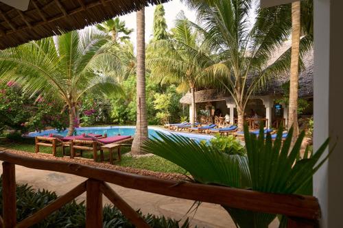 a resort pool with tables and chairs and palm trees at African Bungalows in Nungwi