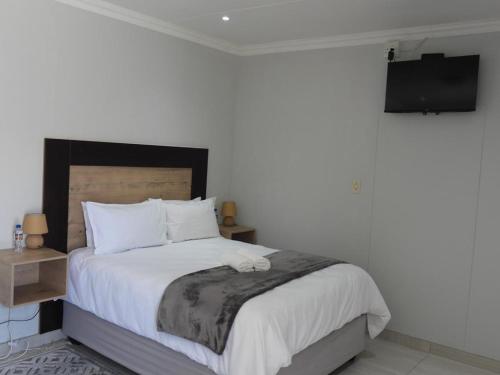 a bedroom with a bed with white sheets and a television at The Shifting Whispering Sands Guesthouse in Walvis Bay