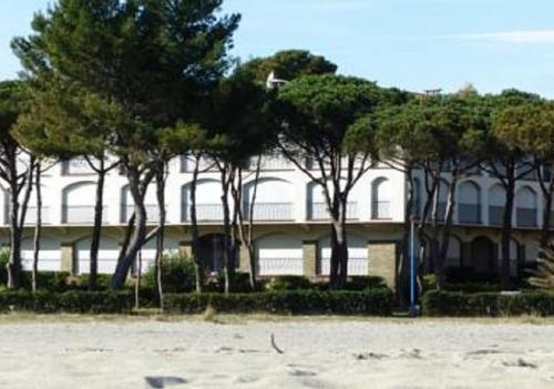 un grand bâtiment blanc avec des arbres devant lui dans l'établissement T2 - Les pieds dans l'eau, à Argelès-sur-Mer