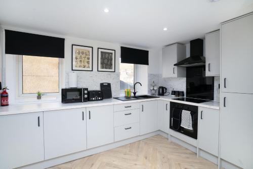 a white kitchen with white cabinets and black appliances at Modern 5 BED-2 BATH Apartment in Galashiels