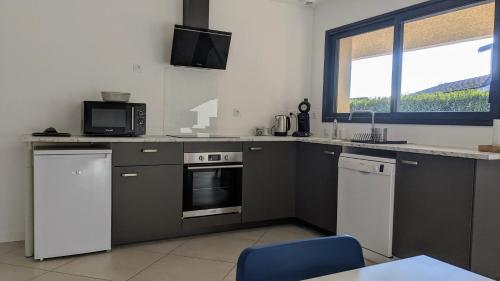 une cuisine avec des placards gris et un four micro-ondes ainsi qu'une fenêtre dans l'établissement #01 - Le 60 - Gîtes modernes et confortables, à Villieu