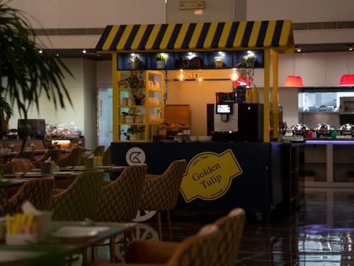 a restaurant with chairs and a counter with a sign on it at Golden Tulip Muscat in Muscat
