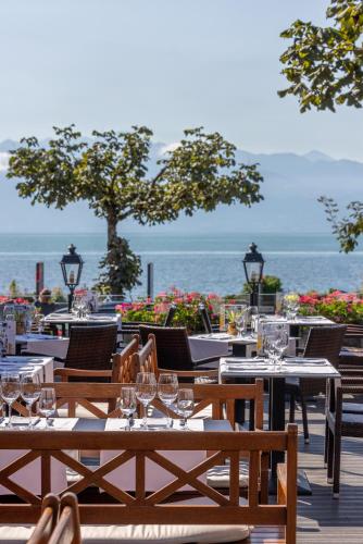 a restaurant with tables and chairs with the ocean in the background at Romantik Hotel Mont Blanc au Lac in Morges
