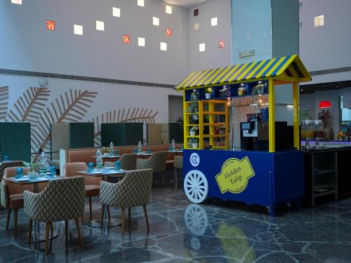 a food cart in a restaurant with tables and chairs at Golden Tulip Muscat in Muscat