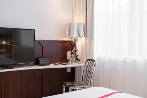 a bedroom with a desk with a television and a chair at Ruby Leni Hotel Dusseldorf in Düsseldorf