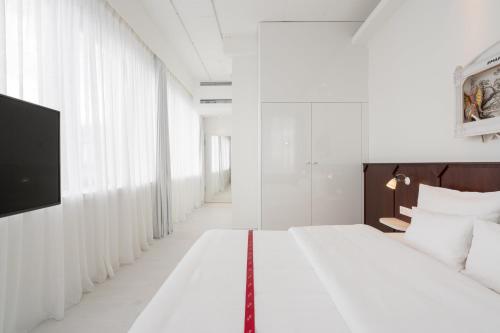 a white bedroom with a large bed and a tv at Ruby Leni Hotel Dusseldorf in Düsseldorf