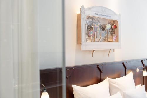 Una cama con almohadas blancas y una foto encima. en Ruby Leni Hotel Dusseldorf, en Düsseldorf