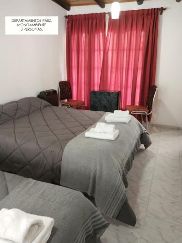 two beds in a room with red curtains at Departamentos PAEZ in Malargüe