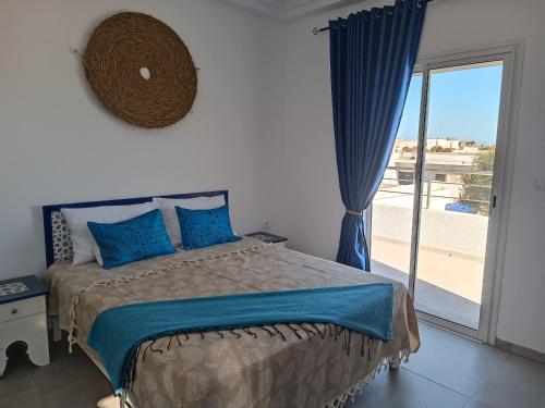 a bedroom with a bed with blue pillows and a window at Villa Evasion Djerba in Awlād ‘Umar