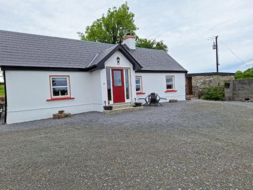 a white cottage with a red door on a gravel driveway at Lough Lea House, Bunnamuca in Strokestown