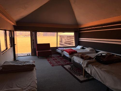 a room with three beds and a chair and windows at Milky Way Wadi Rum in Wadi Rum